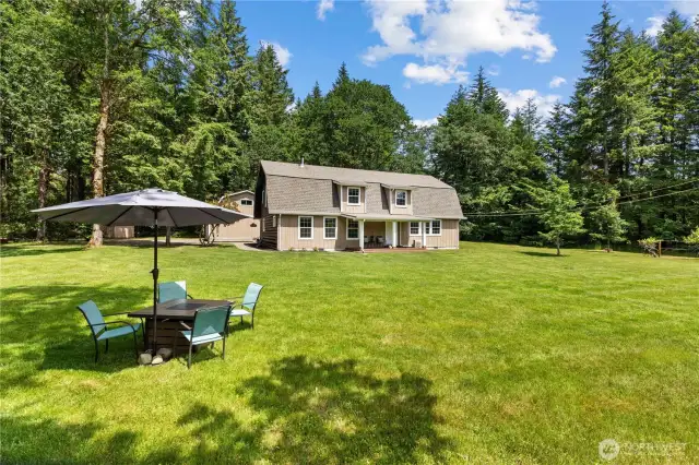 Charming Cabin-Style Home with Expansive Lawn & Outdoor Living  This inviting 2-story home sits peacefully in the center of a lush, open clearing surrounded by towering evergreens. With its classic cabin-style design, covered front porch & charming dormer windows, this home blends rustic appeal with modern updates. The expansive lawn is perfect for entertaining, outdoor dining, or simply relaxing in the quiet of nature. Enjoy morning coffee or evening BBQs in your private Pacific Northwest paradise—just under 10 acres of pure tranquility.