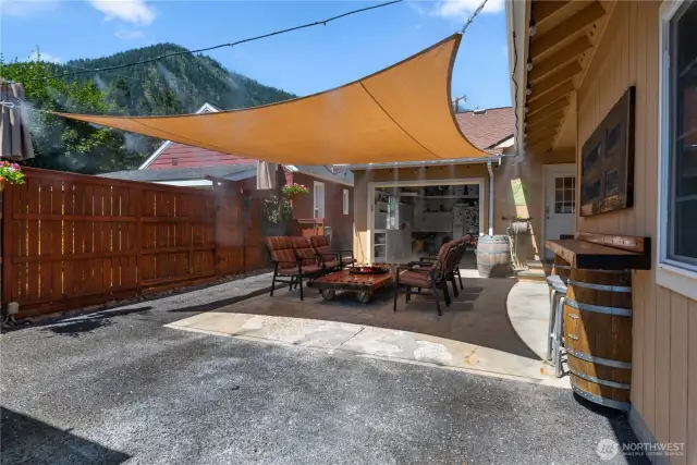 Outdoor rear patio area with misting system and shade sail.  On right, built in bar with seating.  Note the driveway entrance to the single garage is doubling as a patio seating area.  Shade sail and misting system stay with the house.