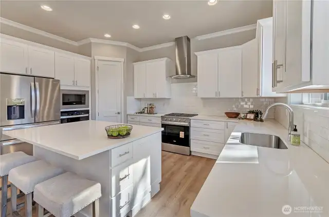 Large kitchen area with oversized island, solid surface, easy to clean quartz counter surfaces, custom white painted cabinetry plus durable hardwood flooring and quality Whirlpool appliances. The perfect area to prepare your meals and snacks and to host get togethers.