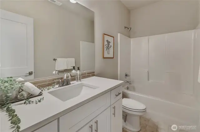 The bathroom area includes white cabinetry, easy to clean quartz surfaces with below mounted sink and tub-shower
