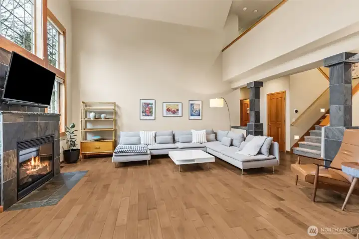 From this angle, the room really shows off its layers. The fireplace becomes more of a focal point, complete with a mounted TV spot above, while those slate wrapped columns quietly tie back to the slate fireplace and add a little architectural weight to the space. The mix of materials feels intentional, wood floors, slate accents, soft walls, all working together without trying to compete. Up above, the second story hallway runs in a catwalk style, open to the room below but with a solid railing that keeps things feeling grounded while still giving that airy loft vibe. You also get a look at the staircase and a deep under stair storage closet that’s ready to hide everything from holiday bins to everyday clutter.