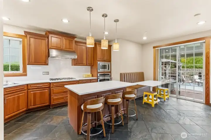 This angle gives you the full working side of the kitchen. The island seating is right up front, perfect for casual meals or keeping the cook company, while the five burner cooktop and stainless hood bring a more serious, chef-ready feel. Across the way, the wall oven and microwave setup keeps everything streamlined and easy to use. The breakfast nook sits just beyond, with a clear view out the sliding glass door to the covered patio and even a peek at the gazebo out back. It all feels connected, easy to move through, and set up for both everyday routines and having people over.