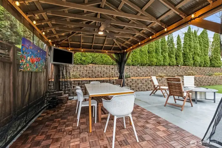 Call this your backyard VIP section. Parquet-style tile flooring sets the tone, the mounted TV stays for instant entertainment, and the bug netting lets you decide how open or cozy you want the space. There’s a ceiling fan to keep things breezy and lighting that carries you straight into evening without packing it in early. It’s set up for everything from quiet lounging to full-on hosting, no extra effort required.