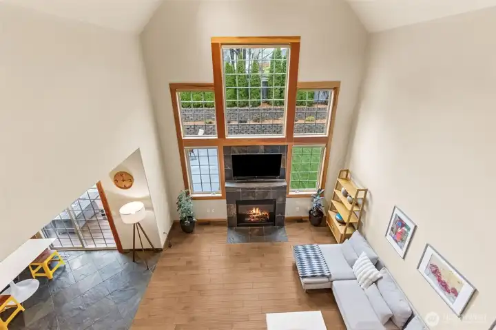 This is the vantage point that really shows off the drama. Looking down from the upstairs catwalk, you get the full effect of that soaring wall of windows and the gas fireplace holding court below. The terraced backyard peeks through all that glass, so even from up here you’re connected to the outdoors. It’s open, it’s bright, and it gives the whole home that “wow, this is a lot of space” feeling in the best way.