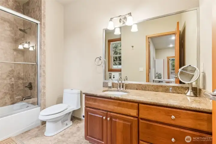 This en suite bathroom is doing exactly what you want it to do, spacious, practical, and quietly polished. The extra long vanity with granite counters gives you plenty of room to spread out, with an undermount sink and brushed nickel fixtures keeping the look clean and classic. Tile floors handle real life with ease, and the glass door tub and shower combo keeps things feeling a little more elevated than your standard setup. The wood wrapped window brings in natural light, and those 9 foot ceilings give the whole space a bit more breathing room. Warm, neutral tones tie it all together in a way that will age well and work with just about any style.