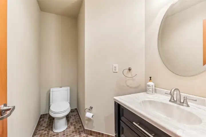 This upstairs powder room is right where you want it, just off the bonus room so guests and game nights stay contained without anyone wandering the house. Eco friendly dual flush toilet, a clean vanity setup, and a beveled round mirror that adds a little polish without overdoing it.