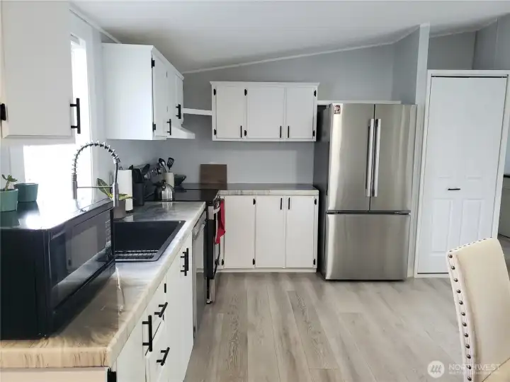 Spacious Open Kitchen showing White Cabinets, New Stainless-Steel Appliances, White Painted Trim, Large Pantry, New Sink, Faucet, Counter Tops, LED Lighting, and Vinyl Plank Flooring.