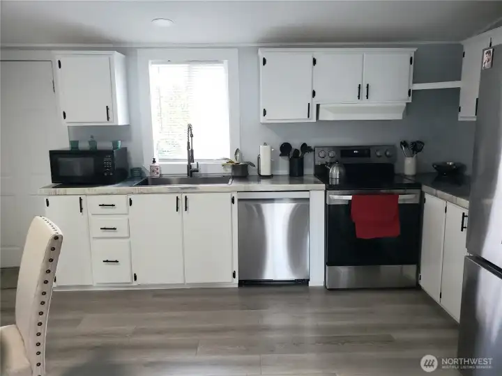 Another Picture of the Spacious Open Kitchen showing White Cabinets, New Stainless-Steel Appliances, White Painted Trim, Large Pantry, New Sink, Faucet, Counter Tops, LED Lighting, and Vinyl Plank Flooring.