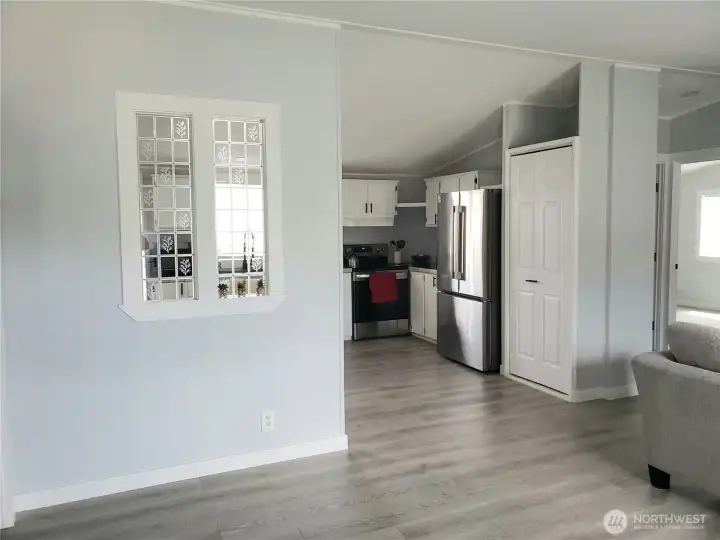 A Picture from the Front Entry Door showing the Living Room and the Spacious Open Kitchen showing White Cabinets, New Stainless-Steel Appliances, White Painted Trim, Large Pantry, New Sink, Faucet, Counter Tops, LED Lighting, and Vinyl Plank Flooring.