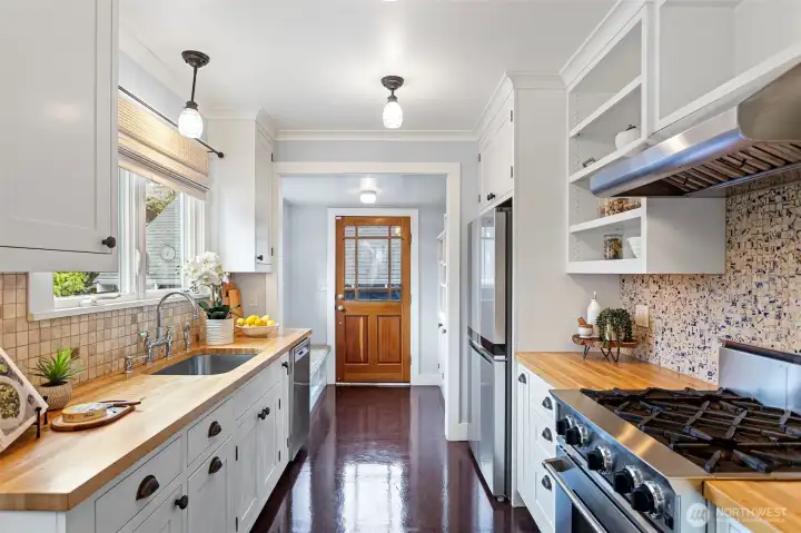 The $100,000 remodel didn't miss. BlueStar range, butcher block, white shaker cabinetry, blue and white ceramic mosaic. Function first — and it shows.