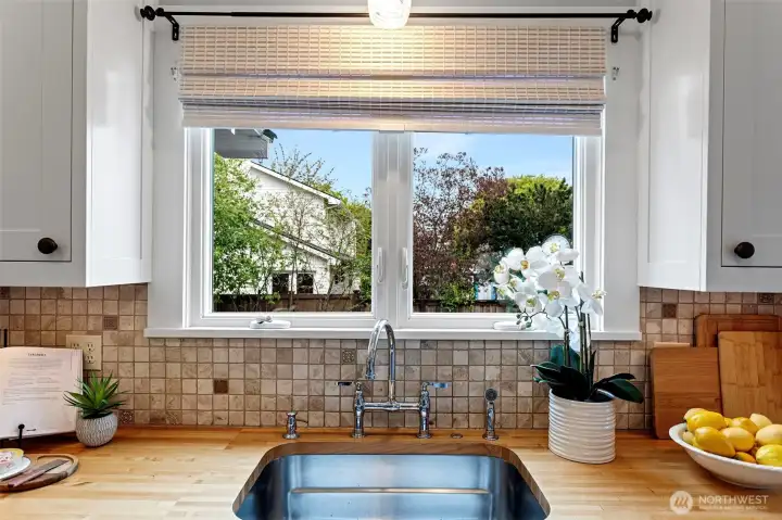Butcher block meets tumbled crema marfil marble at the sink. Chrome bridge faucet, garden window, morning light. The details hold up close.