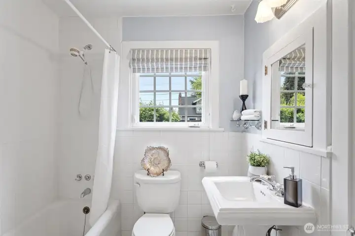 Pedestal sink, chrome cross-handle faucet, white subway tile wainscot, black and white mosaic tile floor with diamond border. The main floor bath didn't try to update itself — and it was right.