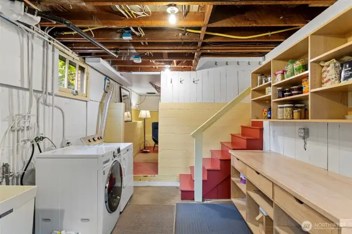 The laundry room does its job. Custom built-in shelving, full-size washer/dryer, utility sink. Down those red stairs: the bonus room.
