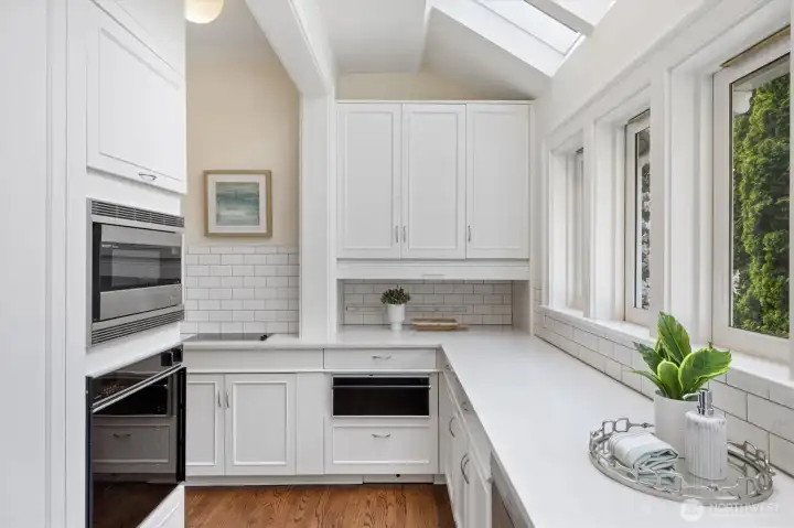 The scullery area is tucked around the corner from the kitchen. Warming drawer, induction burners for caterer or home chef, additional ovens, and walls of cupboards and shelves.