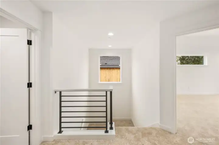 The upper landing provides a bright transition space with a modern metal railing and a window that brings in soft natural light. This open landing creates a comfortable flow between the bedrooms and upstairs spaces.     These photos are from Lot 3 at Gooden Hollow, which is the same floorplan. However, Lot 6 will have changes, so all photos, renderings, site maps, and floorplans are for visualization purposes only. Plans, colors, building orientation, finishes, home outlook, and other details can and WILL vary.
