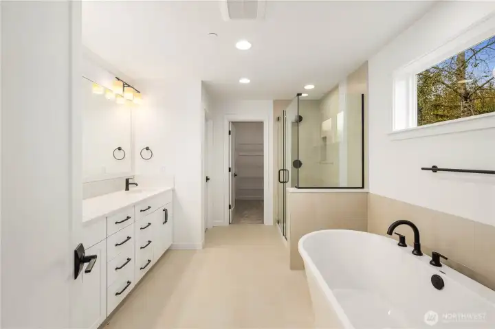 This beautifully designed bathroom features a freestanding soaking tub, dual vanities with abundant storage, and a large glass-enclosed shower. Warm tile tones and modern black fixtures elevate the space into a calming, spa-like experience.    These photos are from Lot 3 at Gooden Hollow, which is the same floorplan. However, Lot 6 will have changes, so all photos, renderings, site maps, and floorplans are for visualization purposes only. Plans, colors, building orientation, finishes, home outlook, and other details can and WILL vary.