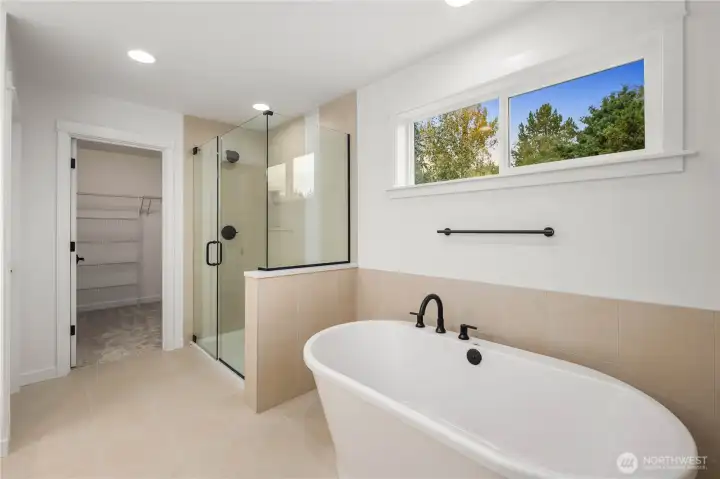 A luxurious walk-in shower with frameless glass and tile surround sits beside a sleek freestanding tub with high windows for no loss of light with added privacy. This layout offers both a spa-like retreat and functional everyday comfort in a beautifully curated design.    These photos are from Lot 3 at Gooden Hollow, which is the same floorplan. However, Lot 6 will have changes, so all photos, renderings, site maps, and floorplans are for visualization purposes only. Plans, colors, building orientation, finishes, home outlook, and other details can and WILL vary.