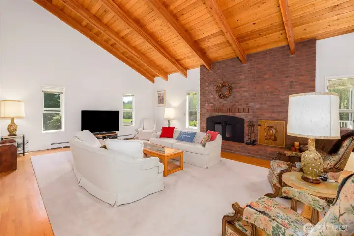 Cozy living room featuring open pine vaulted ceilings and a brick fireplace with doors and fans