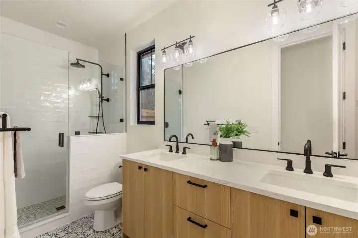 Full bath connected to first floor primary bedroom, glass-enclosed shower with marble accents, and a quartz countertop.