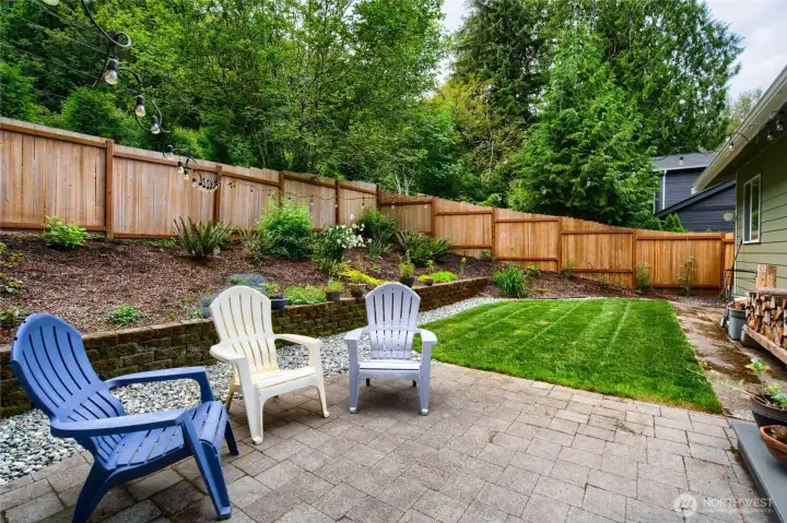 The fully fenced backyard offers a private outdoor retreat with lush landscaping, stone accents, and a spacious patio—perfect for outdoor dining, entertaining, or simply enjoying the tranquil forested setting.
