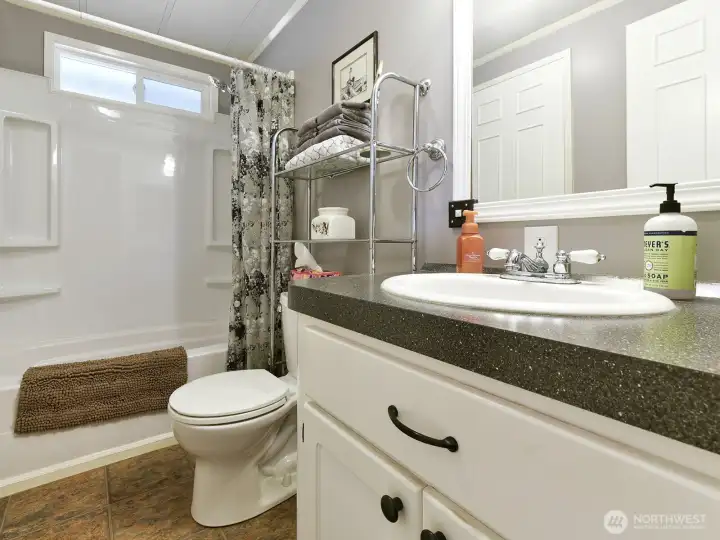 This full bath has continental entry from both the laundry room and the hall for convenient access near the living room and the two bedrooms at one end of the home.