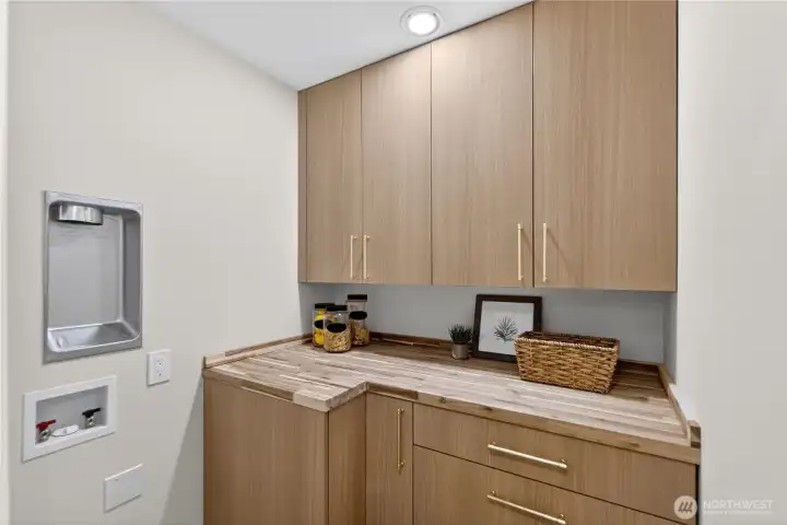 The walk-in pantry continues the same beautiful cabinetry as the kitchen for a cohesive, custom look. A butcher block-style countertop adds warmth and charm, creating a useful space for storage, prep, or small appliances, with stackable washer and dryer hookups tucked conveniently nearby, the same floor as the main bedrooms for convenience. A full size washer and drier set is downstairs as well. The walk-in pantry continues the same beautiful cabinetry as the kitchen for a cohesive, custom look. A butcher block-style countertop adds warmth and charm, creating a useful space for storage, prep, or small appliances, with stackable washer and dryer hookups tucked conveniently nearby, the same floor as the main bedrooms for convenience. A full size washer and drier set is downstairs as well.