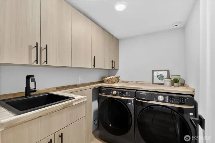 Even laundry feels elevated in this beautifully finished downstairs space, with full-size new Samsung front-load washer and dryer, cabinetry that matches the kitchen, and a warm butcher block-style counter just like the upstairs pantry. Sleek black cabinet handles add a refined designer touch, while the matching deep sink makes delicate washing, soaking, and rinsing easier. With room to fold, sort, and care for the little things, this laundry room turns a daily chore into a space that feels calm, organized, and unexpectedly lovely. Even laundry feels elevated in this beautifully finished downstairs space, with full-size new Samsung front-load washer and dryer, cabinetry that matches the kitchen, and a warm butcher block-style counter just like the upstairs pantry. Sleek black cabinet handles add a refined designer touch, while the matching deep sink makes delicate washing, soaking, and rinsing easier. With room to fold, sort, and care for the little things, this laundry room turns a daily chore into a space that feels calm, organized, and unexpectedly lovely.
