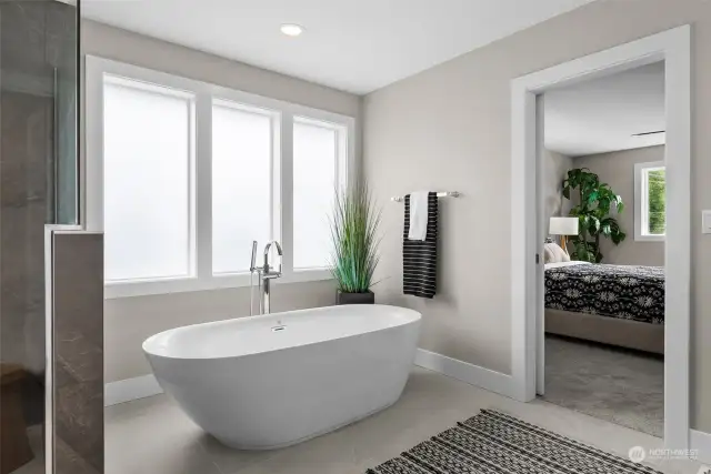 A free standing tub is surrounded by obscured glass windows and oversized floor tiling offering an understated elegance.