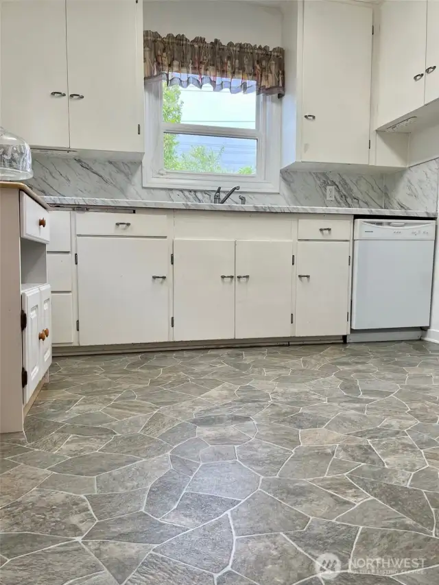 This view of the kitchen from the doorway of the door to the downstairs garage & shop space shows how large the counter space is and how many cabinets there are to make this a kitchen lover's delight