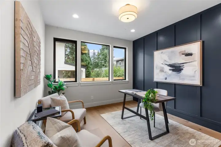 This stylish den offers a perfect blend of comfort and productivity, anchored by a bold accent wall and a sleek wooden desk setup. Natural light pours through the large windows, brightening the space and complementing the warm wood tones and soft textures. With cozy seating and curated decor, it’s an ideal retreat for reading, working, or simply unwinding.
