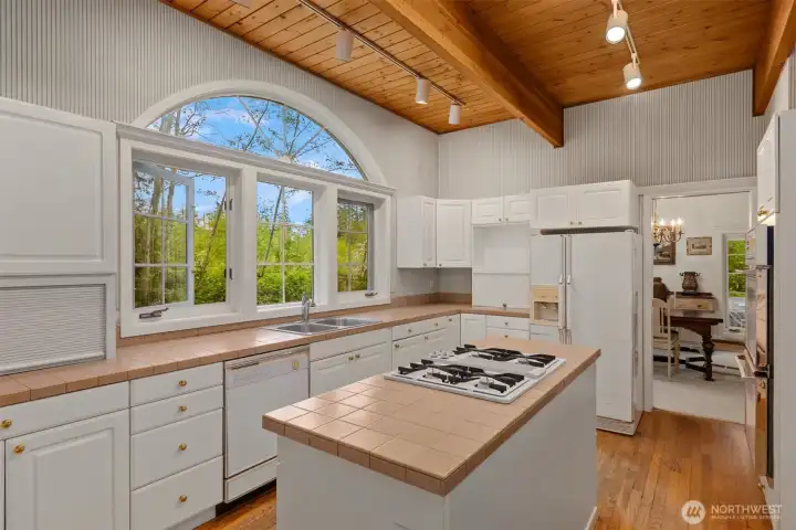 The wood floors and ceiling detail continue into the large kitchen. Custom windows overlook the verdant back yard.