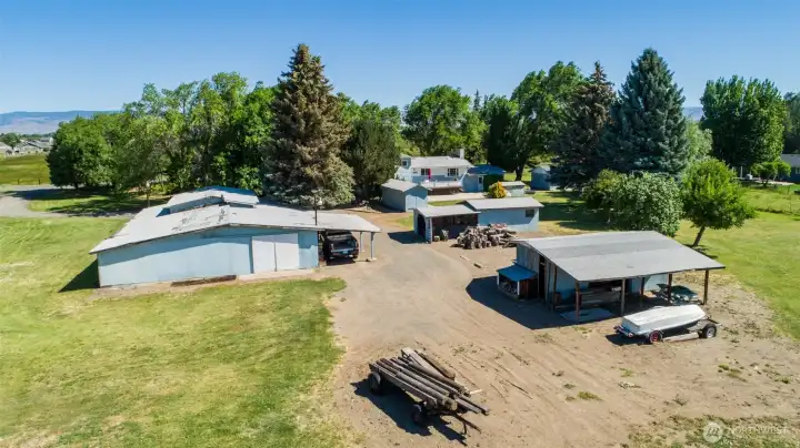 Here is a view from the east of the property. You can see the large shop with a covered parking area and another outbuilding with a covered parking area. Lots of storage at this amazing property. Here is a view from the east of the property. You can see the large shop with a covered parking area and another outbuilding with a covered parking area. Lots of storage at this amazing property.