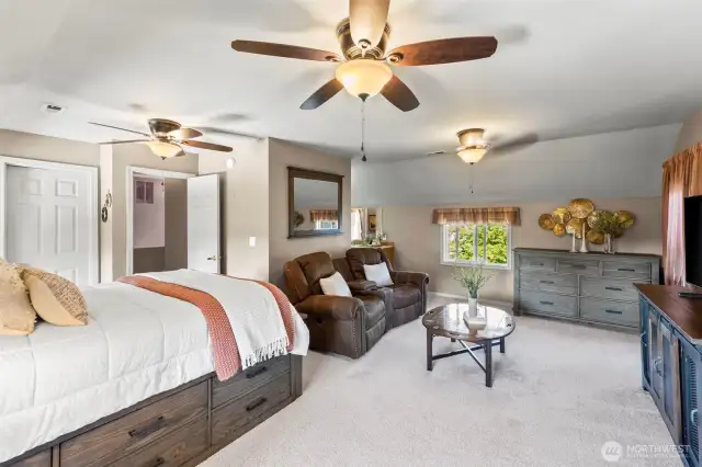 Primary suite with walk in closet, ceiling fans, sitting space, and an electric fireplace.