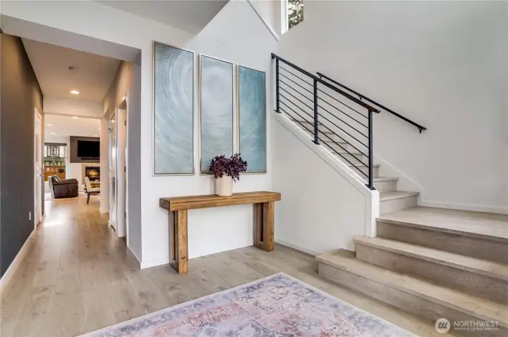 Welcoming entry with soaring vaulted ceiling, abundant natural light, upgraded staircase, and a striking accented wall.