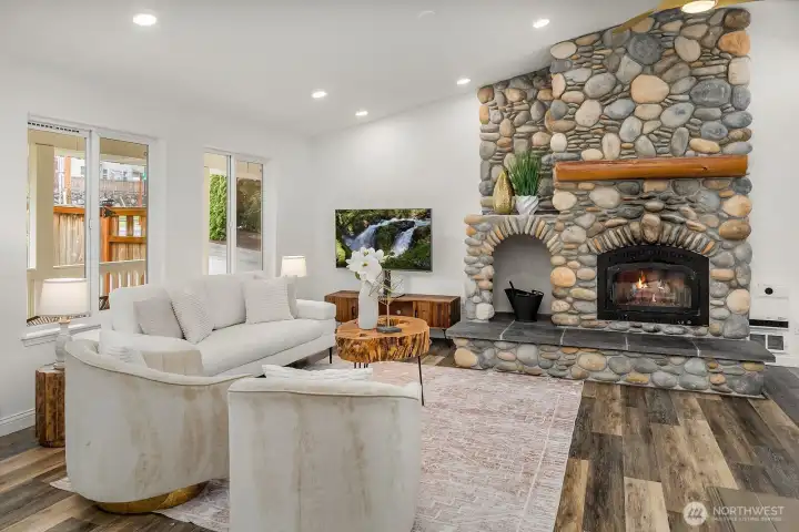 The spacious living area impresses with vaulted ceilings, a stunning floor-to-ceiling stone wood burning fireplace, and warm bamboo flooring, creating an inviting gathering space that perfectly balances rustic charm and modern comfort.