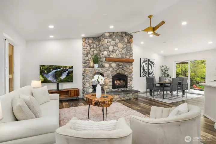 Another angle of the light-filled living room highlights the soaring vaulted ceilings, smart recessed lighting, and the magnificent stone fireplace, with views through to the backyard reinforcing the seamless indoor-outdoor flow this home offers.