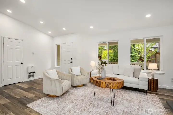 The bright and airy living space showcases fresh white walls, smart recessed lighting, and beautiful bamboo flooring, with a large window framing lush garden views and filling the room with natural light.
