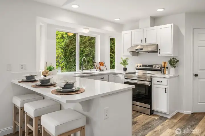 This angle showcases the kitchen's generous island, abundant cabinetry, and newer stainless appliances, with a large garden window bringing the lush backyard greenery right into the heart of the home.