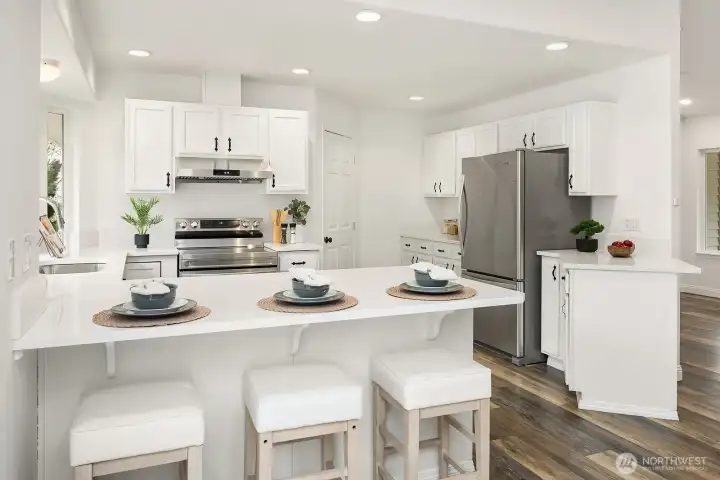 The kitchen's quartz countertops and crisp white cabinetry gleam under recessed lighting, with the spacious island offering generous prep space and casual seating perfect for weeknight dinners and weekend gatherings alike.