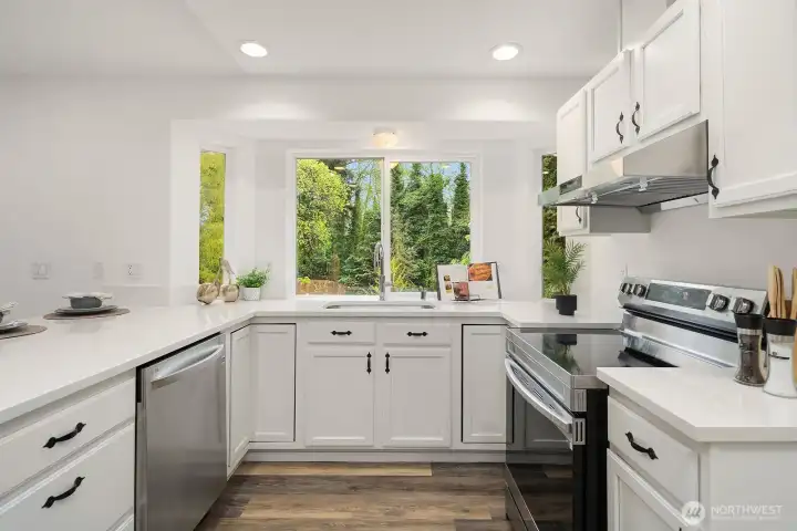 The well-appointed kitchen offers a classic U-shaped layout with ample counter space, newer appliances, and a bright window framing serene garden views, making meal prep a pleasure in this move-in ready home.