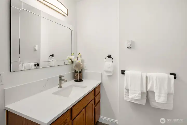 A clean and well-appointed bathroom features warm wood cabinetry, a crisp white vanity, and stylish matte black fixtures, reflecting the thoughtful updates and move-in ready condition found throughout this exceptional home.