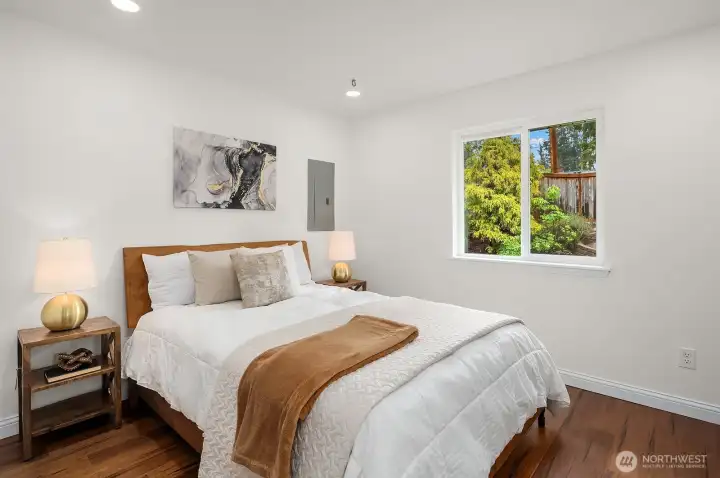 A bright and comfortable secondary bedroom features fresh paint, warm bamboo flooring, and a lovely window with garden views, offering a welcoming retreat for family or guests in this beautifully updated home.