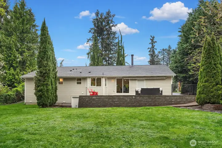 The rear exterior showcases the home's generous lot, lush lawn, and mature landscaping, with the expansive patio just off the main living areas providing a seamless transition to this private and beautifully maintained outdoor space.