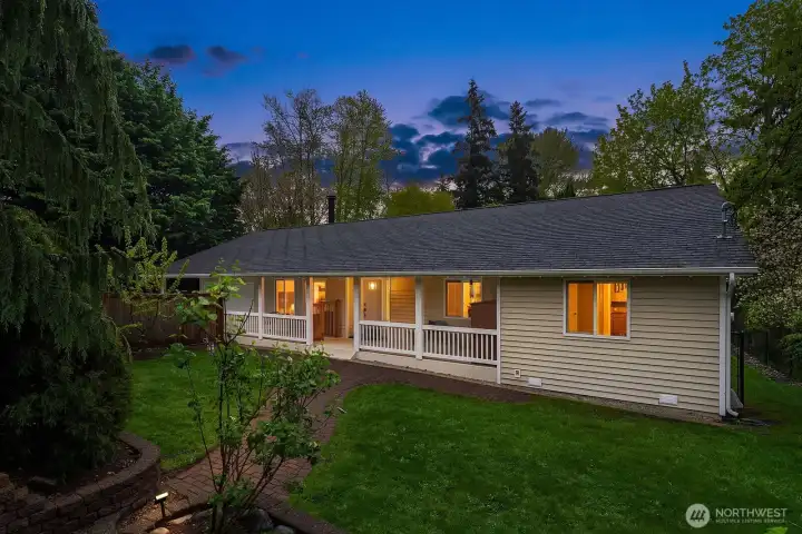At dusk, the home's covered front porch and warm exterior lighting glow invitingly against the twilight sky and mature tree canopy, capturing the timeless charm and exceptional curb appeal of this one-of-a-kind .771 acre property.