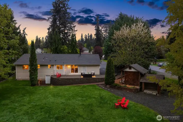 A breathtaking twilight view captures the full magic of this property, with warm lights glowing from the main house and outbuilding alike, the lush lawn stretching out beneath a canopy of mature trees — a truly enchanting setting that brings this exceptional .771 acre estate to life.