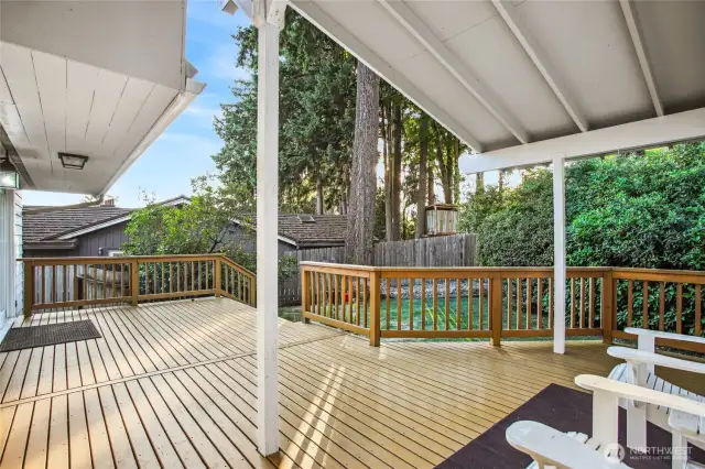 Sweeping deck with all new paint and covered patio overlooks serene backyard.