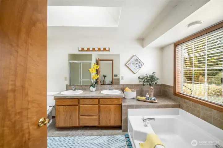 The primary bathroom features a skylight and an easy entry soaking tub with tile surround and flooring.