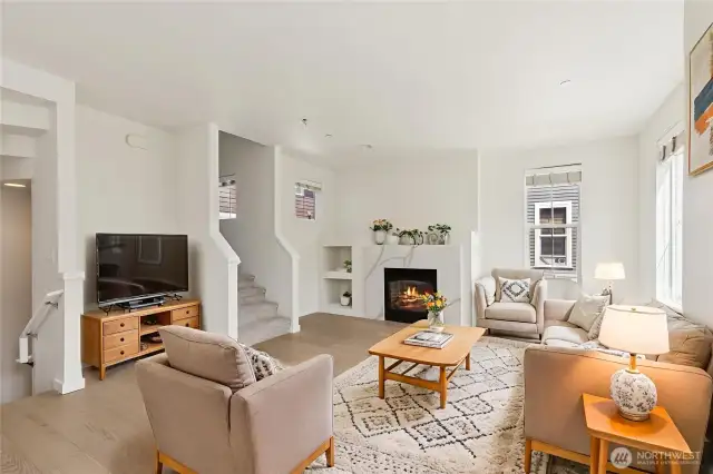 Light-filled open-concept living space featuring a cozy gas fireplace, perfect for both entertaining and everyday comfort. Seamless flow connects living, dining, and kitchen areas in an inviting modern layout.
