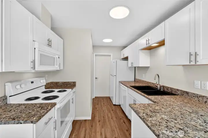 Bright galley-style kitchen featuring granite countertops, abundant cabinet storage, updated white cabinetry, and durable flooring. Efficient layout offers excellent prep space and easy access to the dining and living areas for everyday convenience.