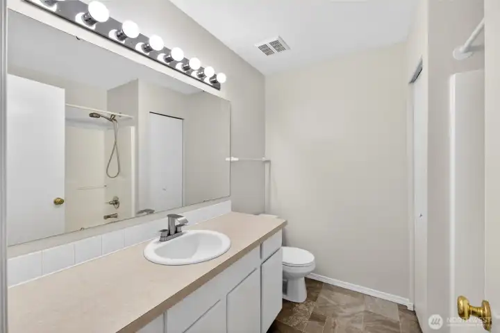Primary bathroom with oversized vanity, expansive mirror, and full tub/shower combination creates a clean, functional space with excellent everyday usability. Neutral finishes and adjacent walk-in closet access add to the comfort and convenience of the primary suite.